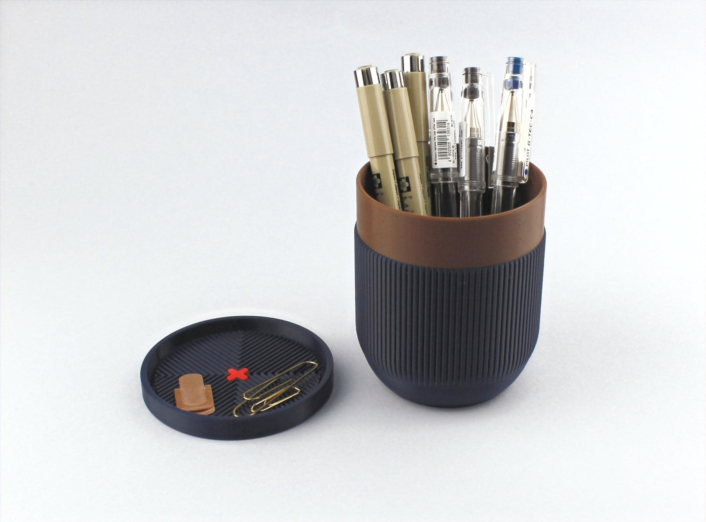 A two-part 3D printed pen holder in blue with a lid, containing various pens and pencils. The lower part serves as a small tray.