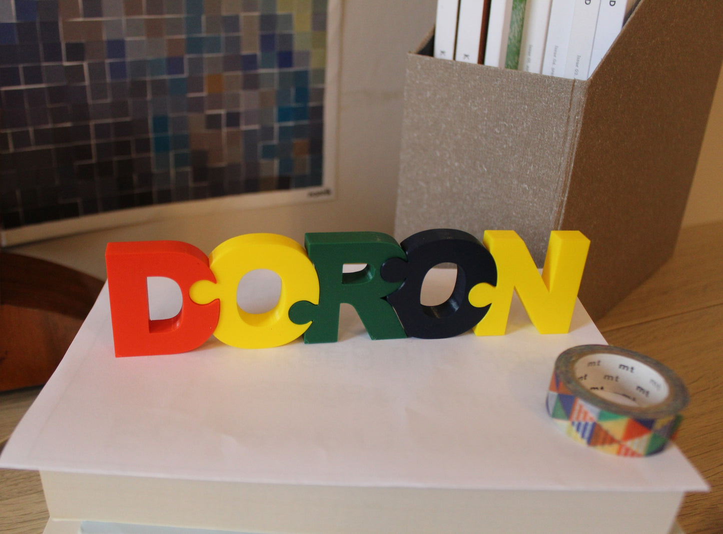 A puzzle of the name Doron standing on a book on a desk