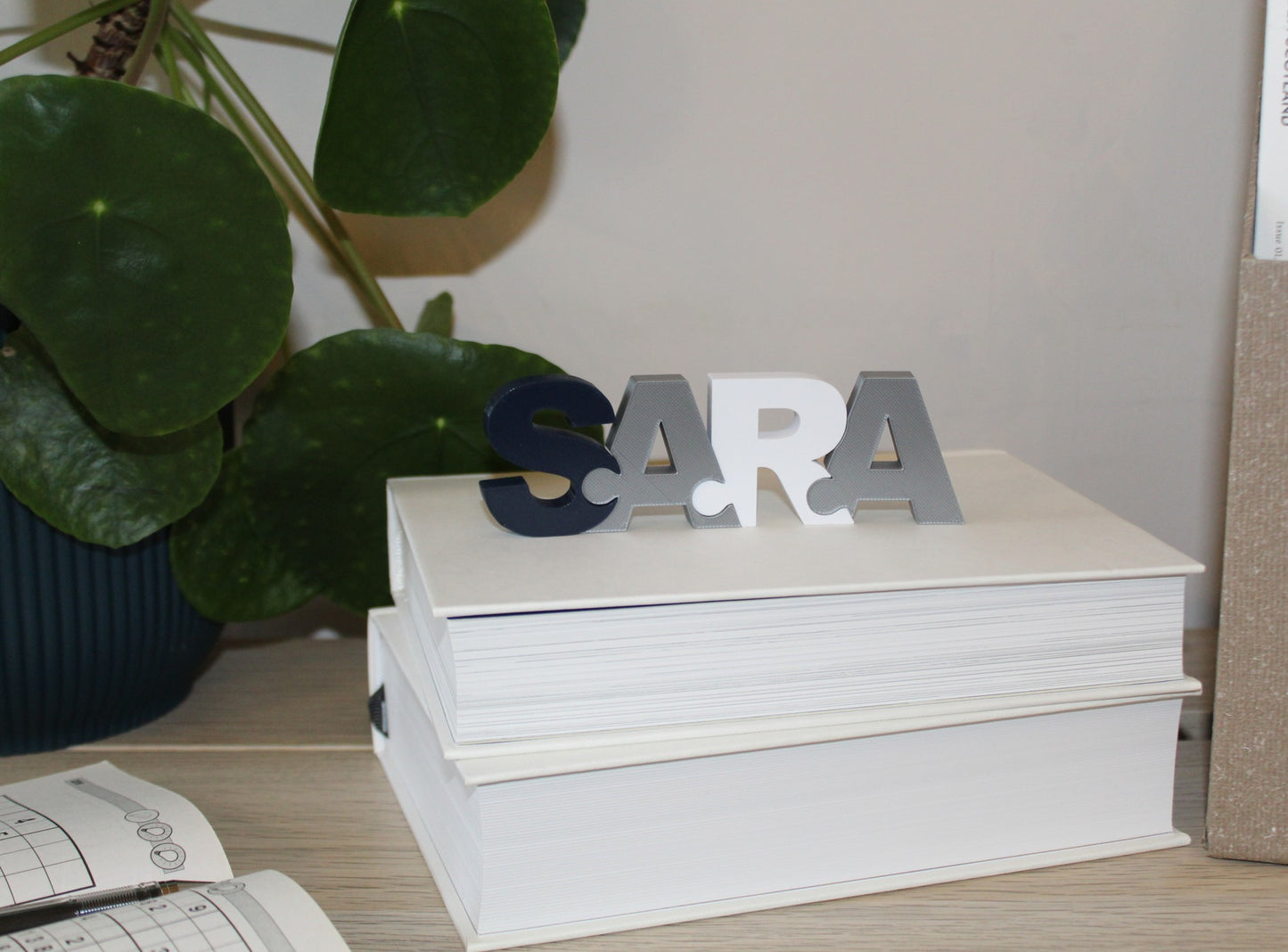 A puzzle of the name Sara standing on a book on a desk