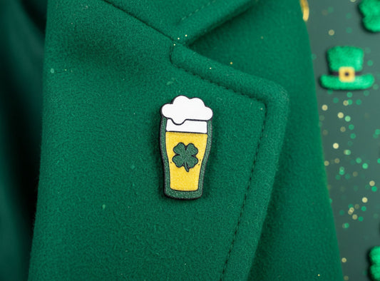 Lapel Pin of a beer glass with a white foam top and green shamrock on a light gray background