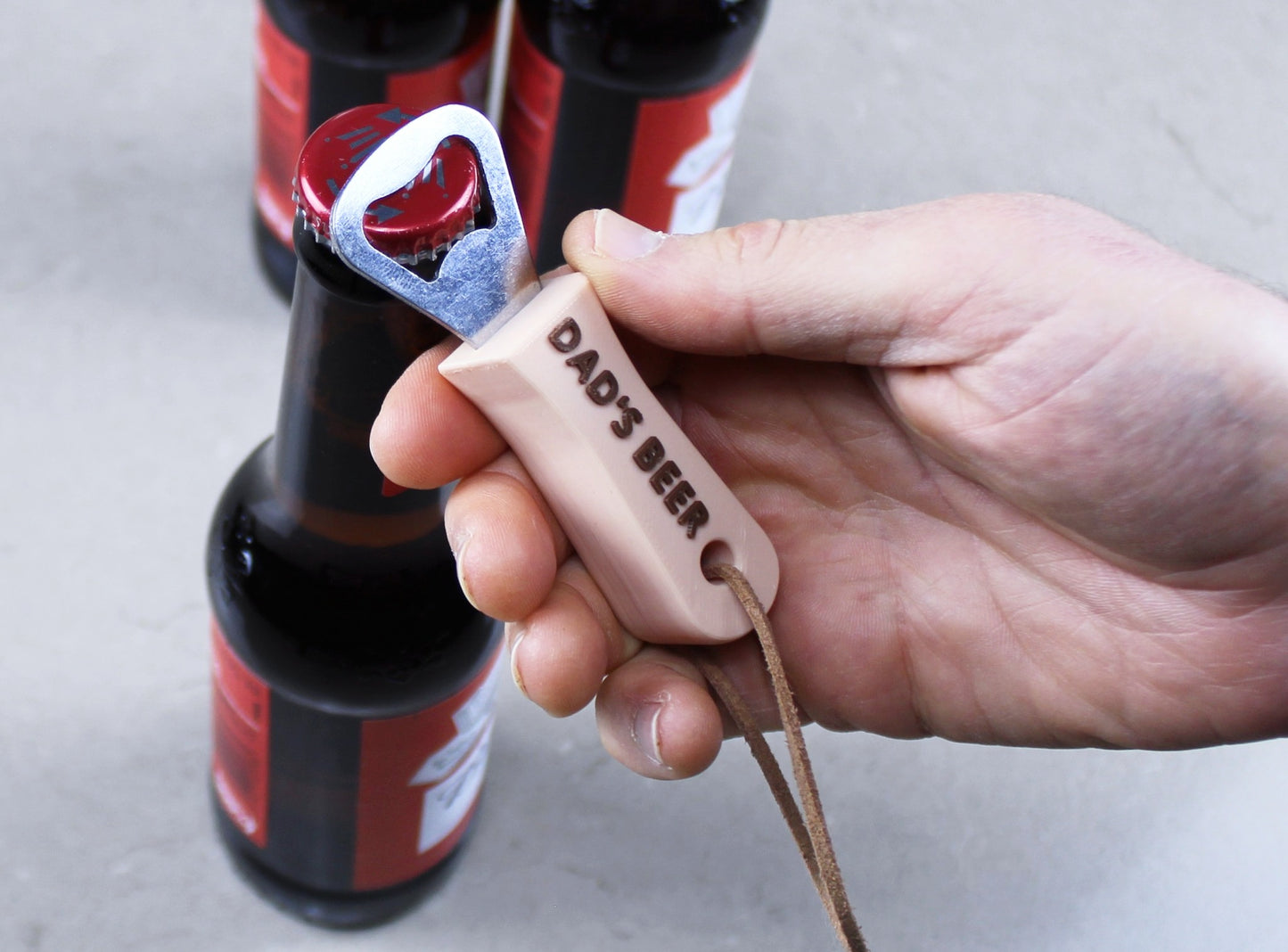 Beige Personalised Bottle Opener with the inscription DAD'S BEER in Brown, held over a beer bottle
