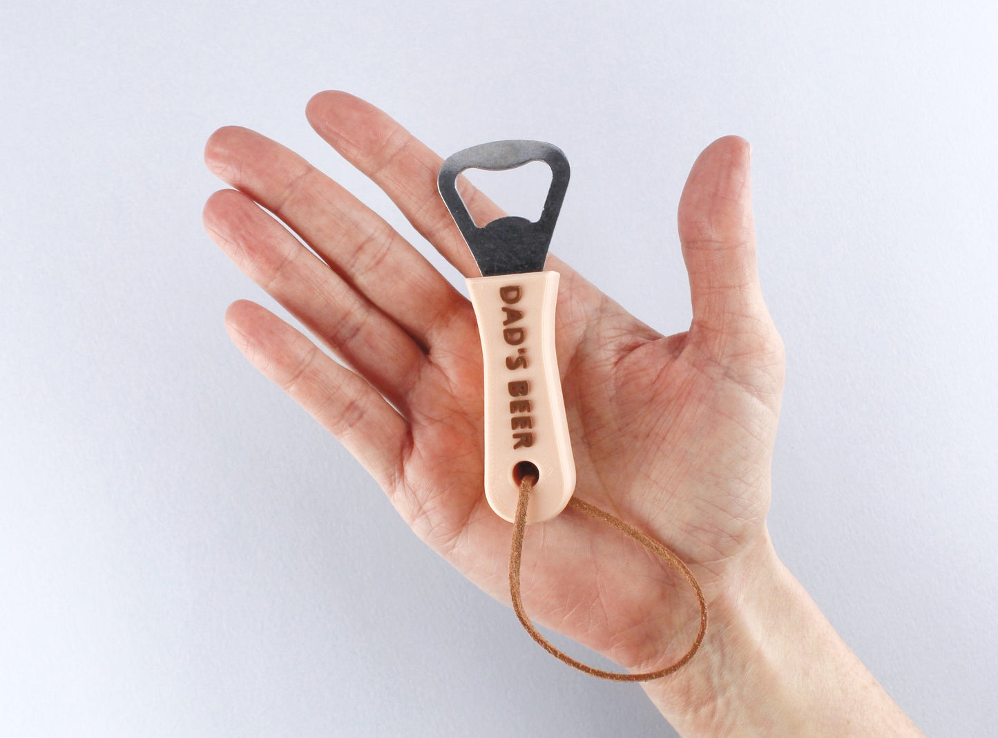 Beige Personalised Bottle Opener with the inscription DAD'S BEER in Brown, placed on an open palm