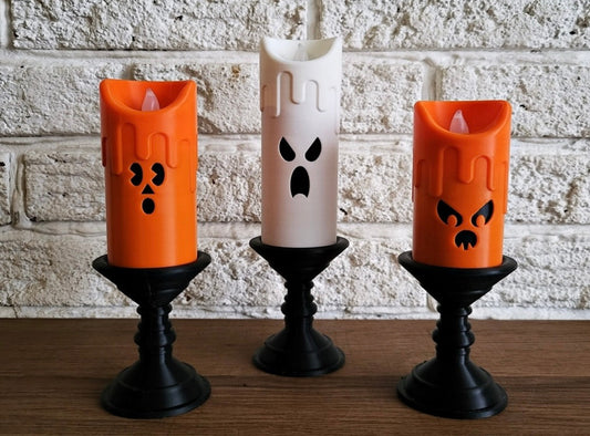 Three Halloween-themed LED candles on black stands against a brick wall.