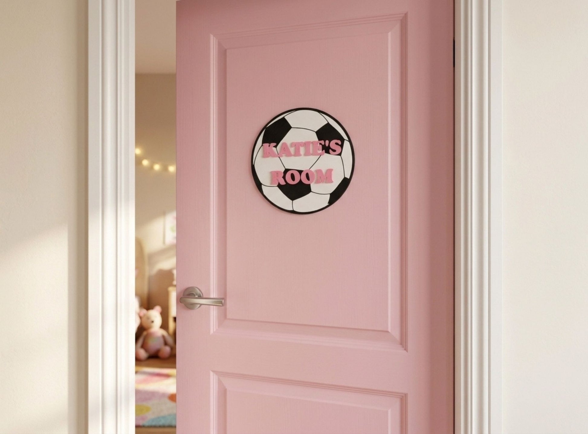 Pink door with a room sign featuring a soccer ball design and the text 'Katie's Room'.
