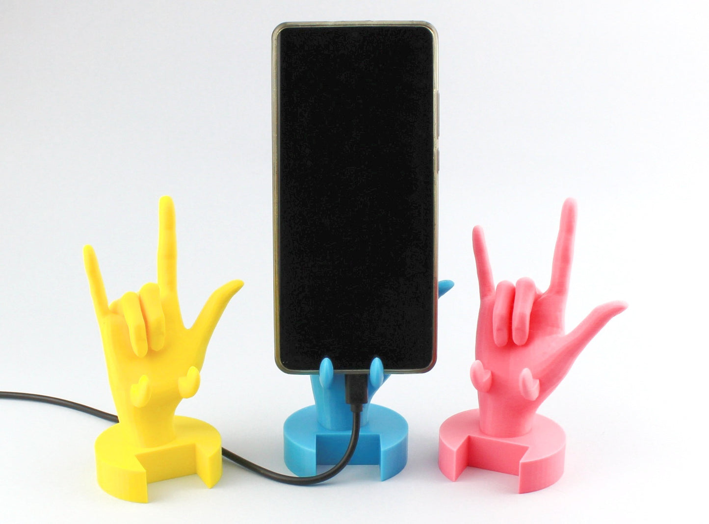 A Yellow, Pink and Light blue 3D Printed I Love You Sign Language Phone Holders and a phone