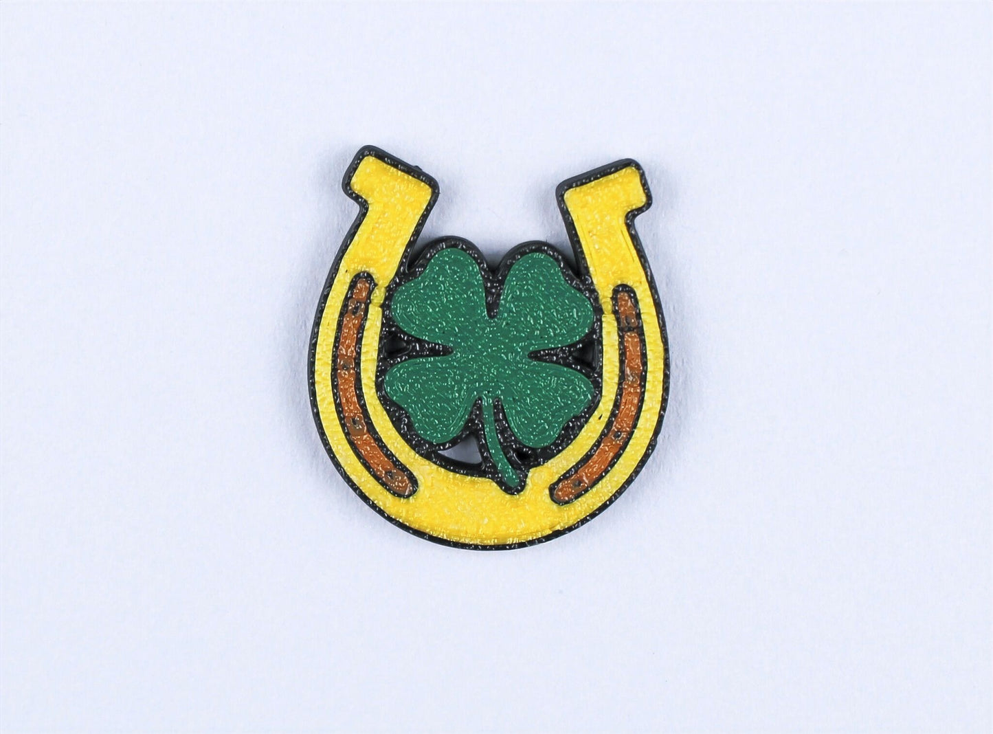 Horseshoe lapel pin with a four-leaf clover on a light grey background