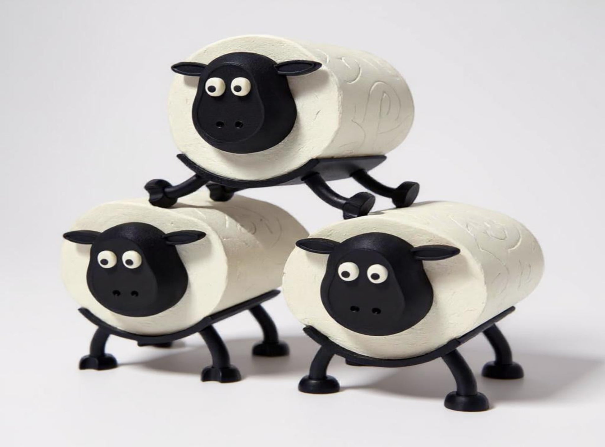 Three sheep-shaped toilet paper roll holder on a stand against a white background