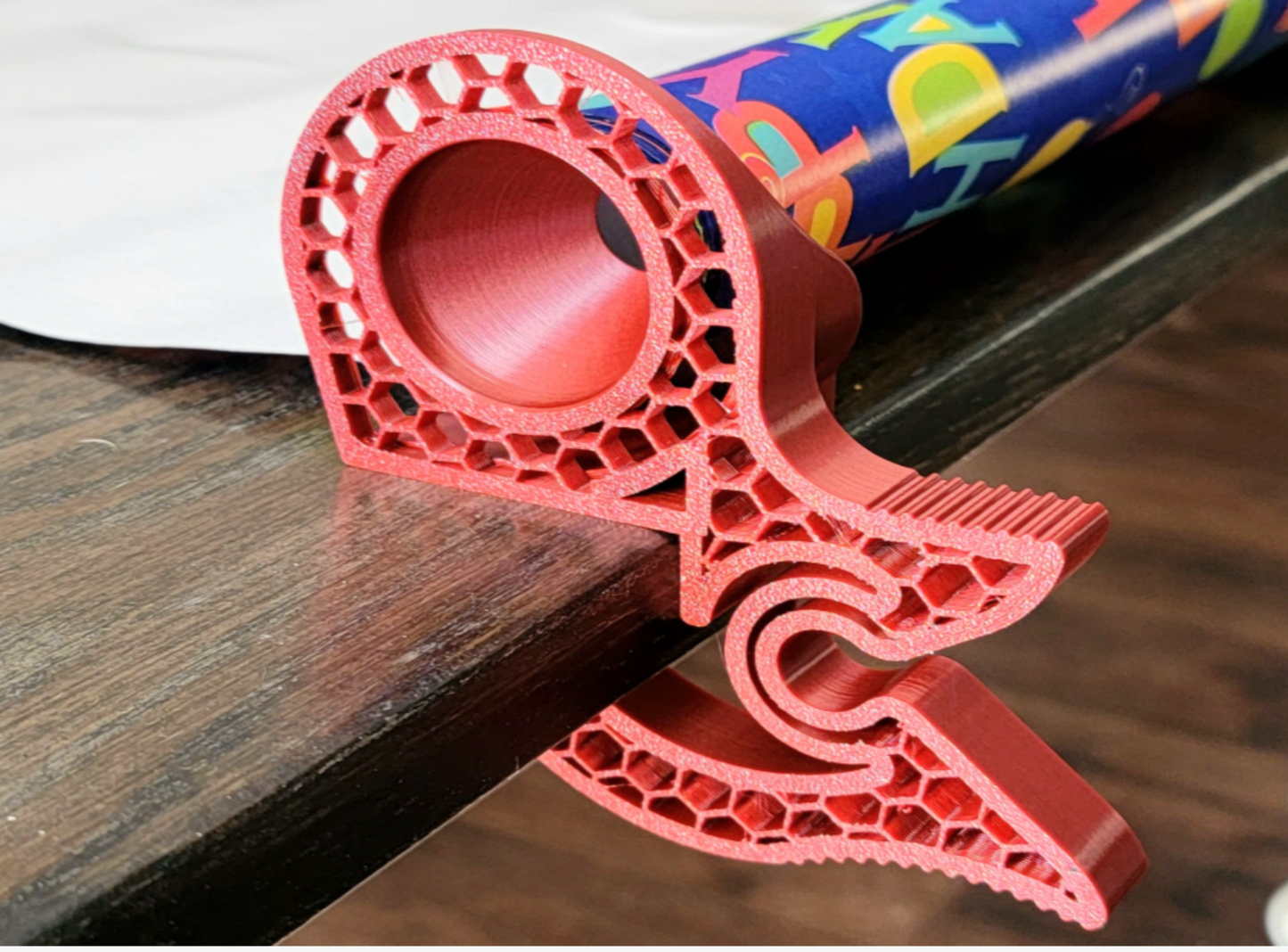 Red 3D-printed Tabletop Gift Wrap clip on a wooden surface with colorful packaging paper