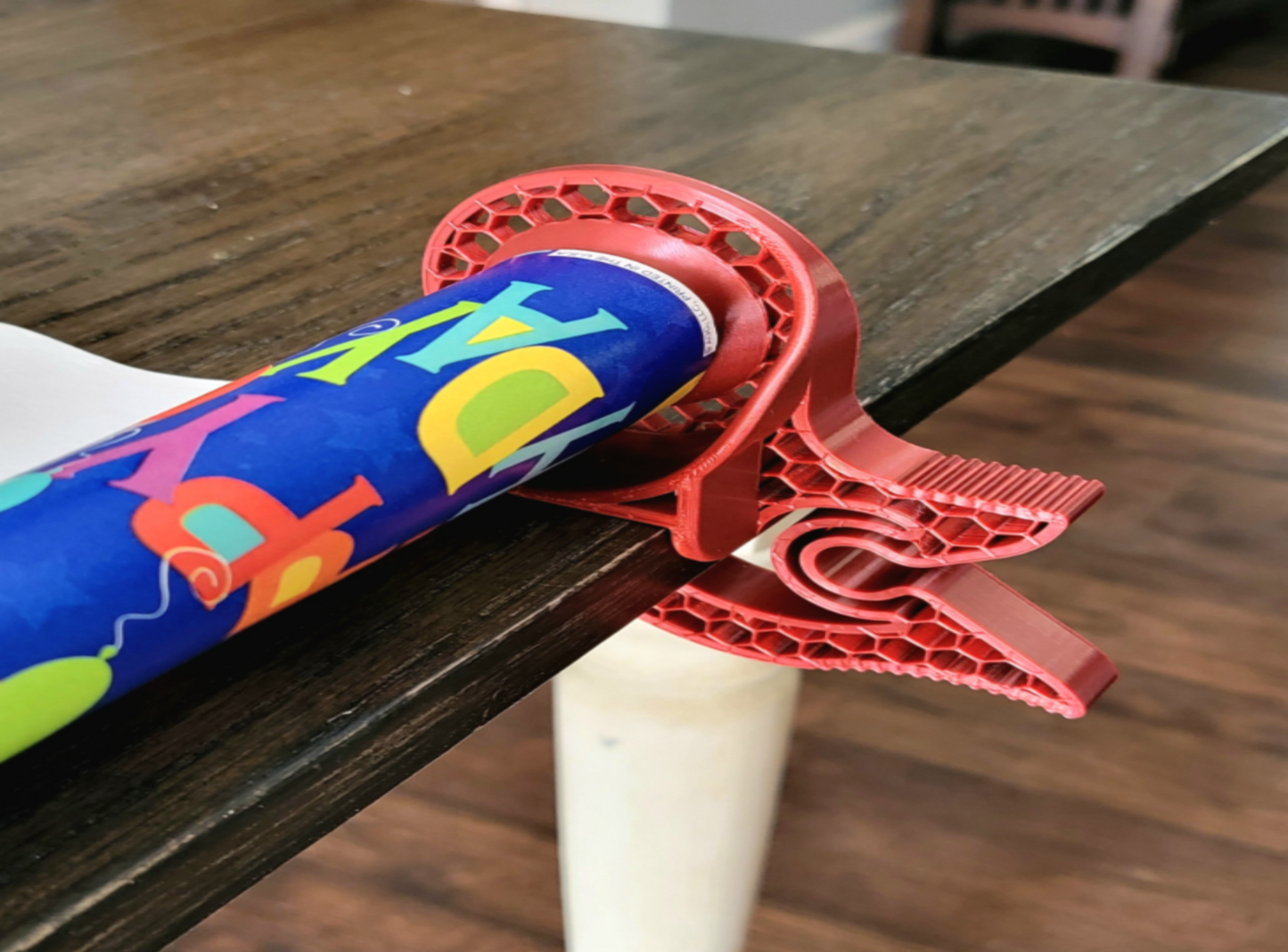 Red 3D-printed Tabletop Gift Wrap clip on a wooden surface with colorful packaging paper