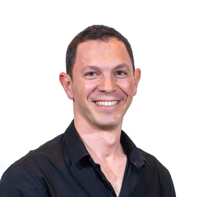 Doron Finkelstein smiling, wearing a black button-down shirt, white background