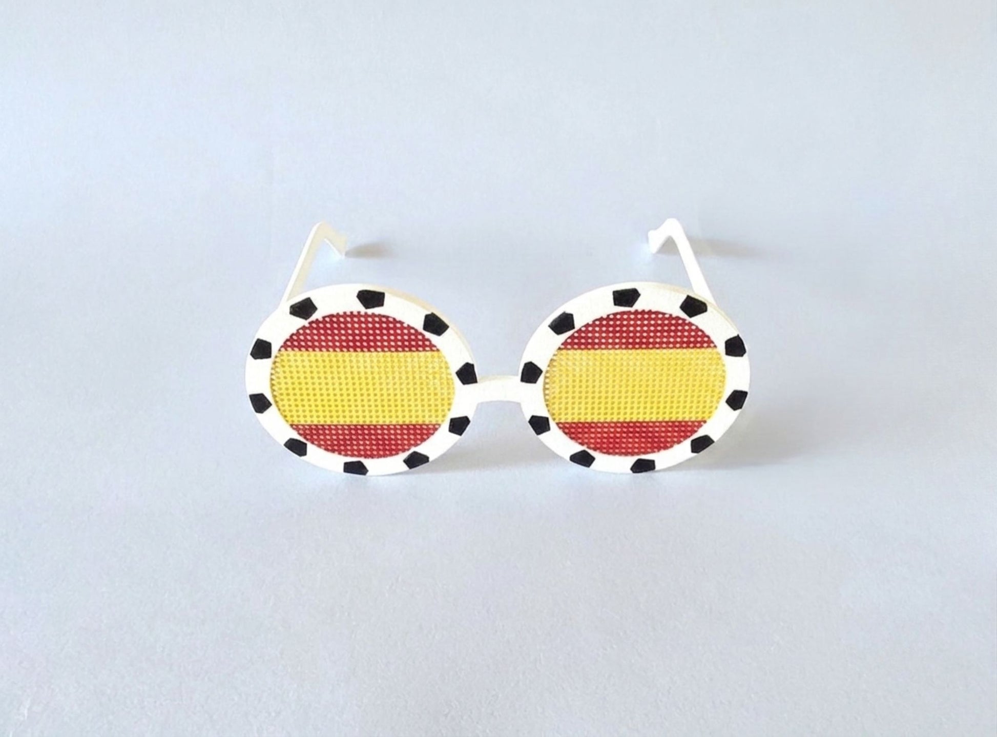 Sunglasses with a Spanish flag design on a light gray background
