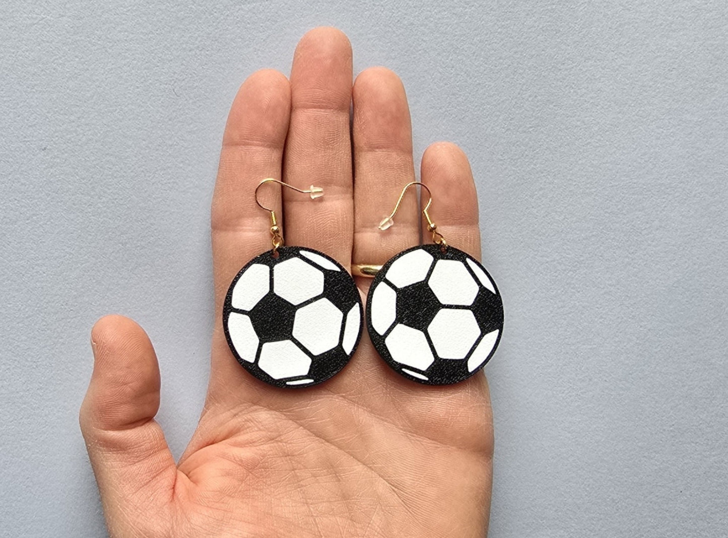 Soccer ball earrings held in a hand against a gray background