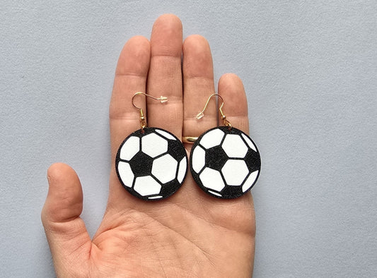 Soccer ball earrings held in a hand against a gray background