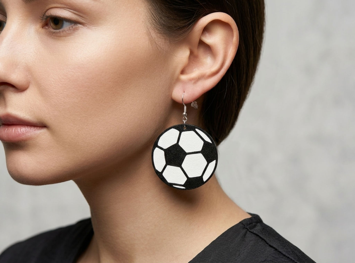 Close-up of a person wearing football earring against a neutral background