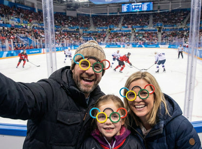 Family with Olympic-themed glasses at an ice hockey game in a stadium.