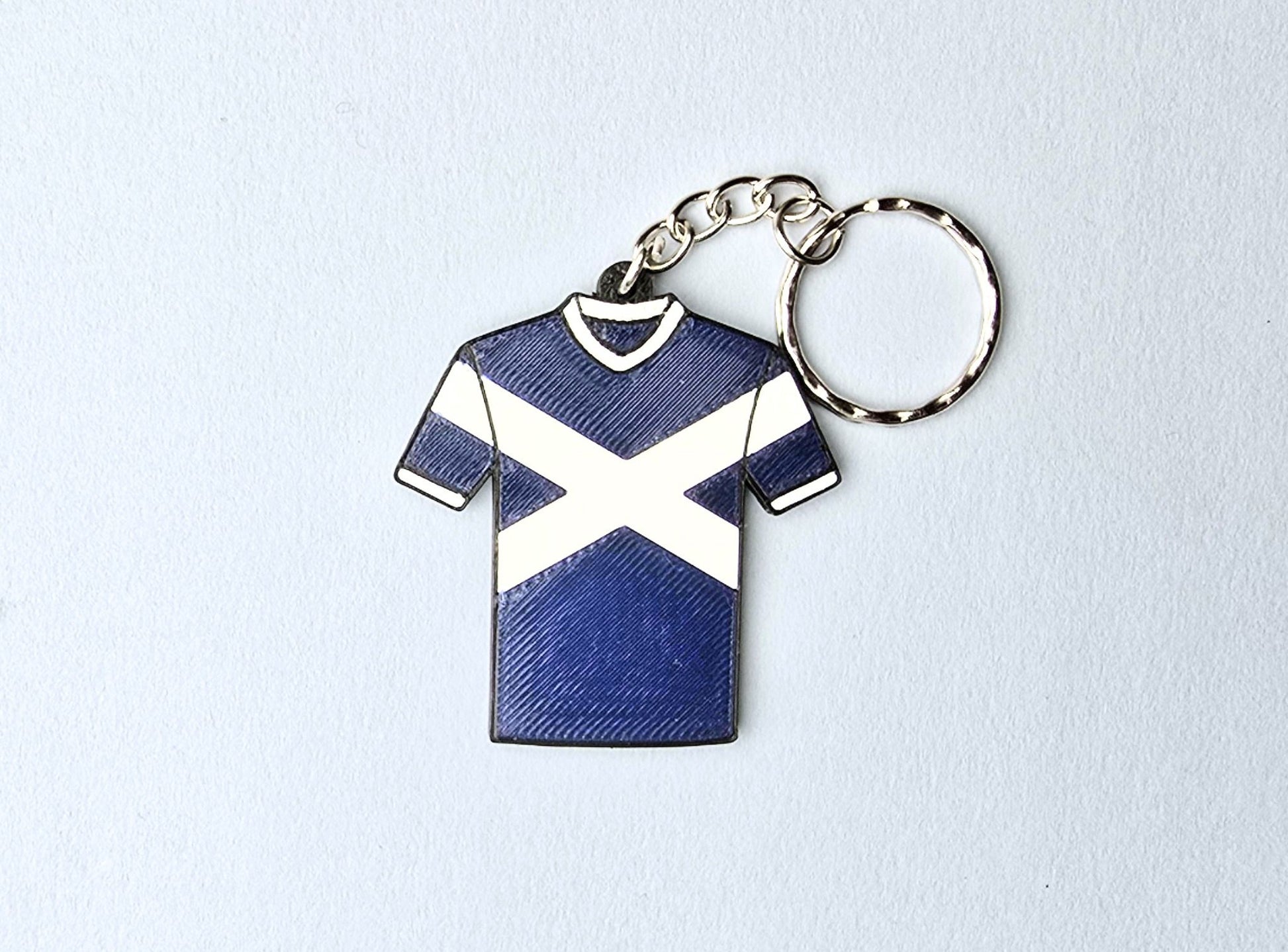 Keychain shaped like a blue and white shirt with a saltire on a light gray background
