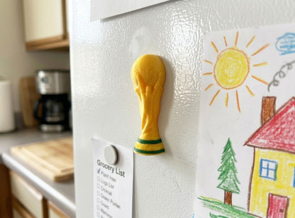 World Cup Trophy-shaped magnet on a refrigerator with a child's drawing of a house and sun.